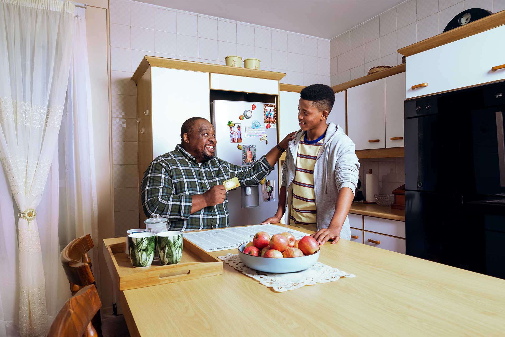 father holding nedbank credit card with his son in the kitchen