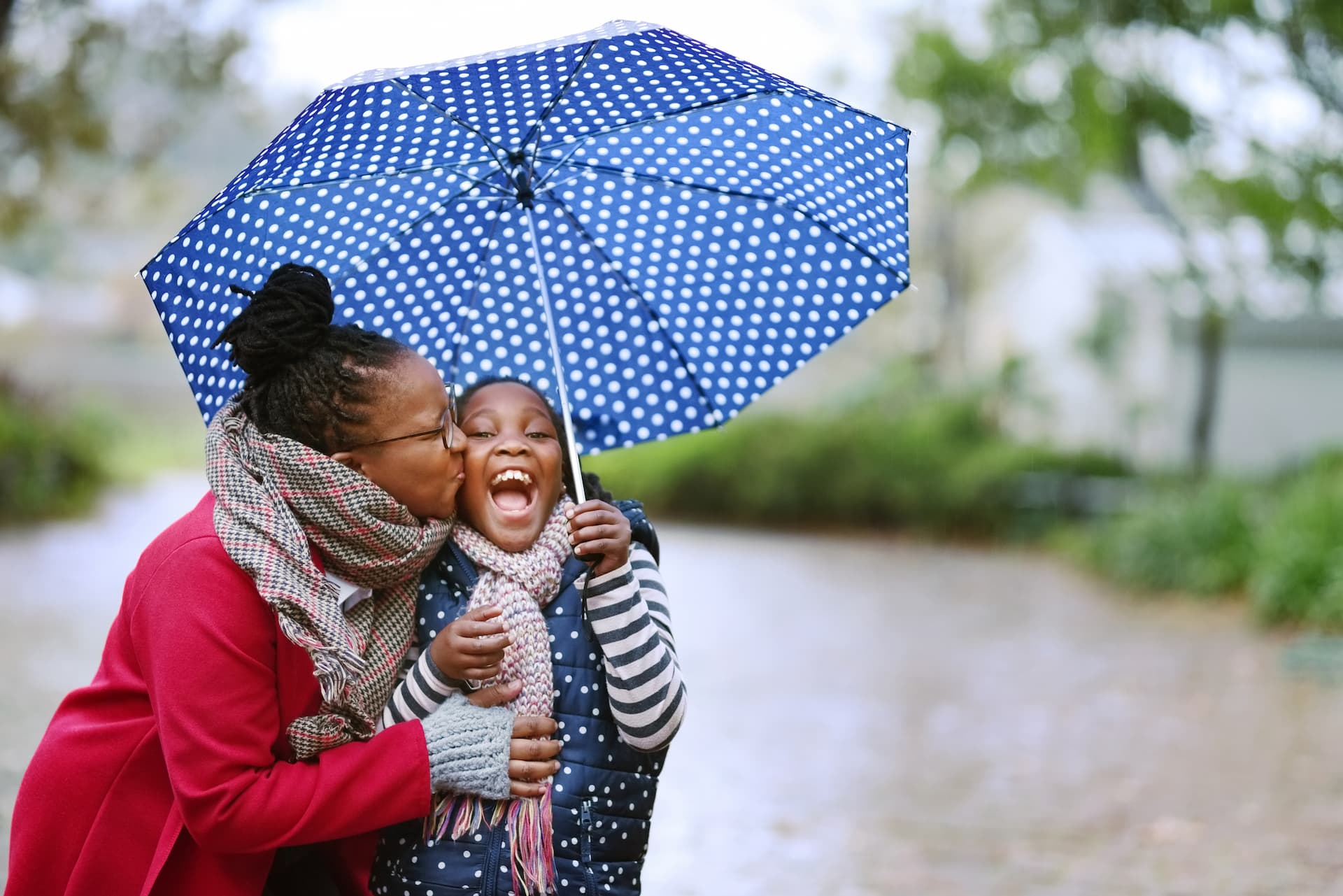 Woman kissing daughter's cheek under umbrella